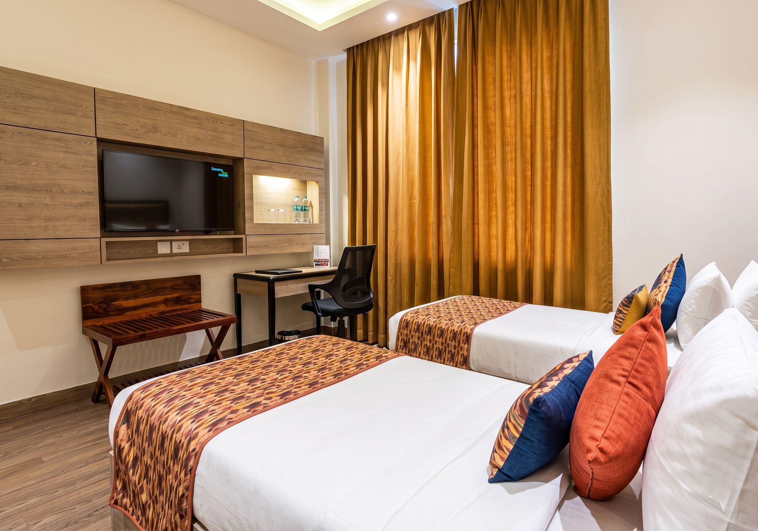 Ein Hotelzimmer mit zwei Betten, einem Schreibtisch, einem Sessel, einem Fernseher und einem Vorhang.