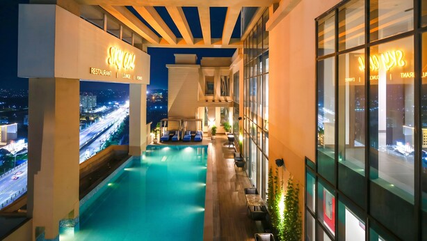 A rooftop pool area with a view of the city at night, a restaurant sign, and a lounge area. - Rhythm Gurugram, Hotel & Suites, Sohna Road - Sector 68 (Gurugram)