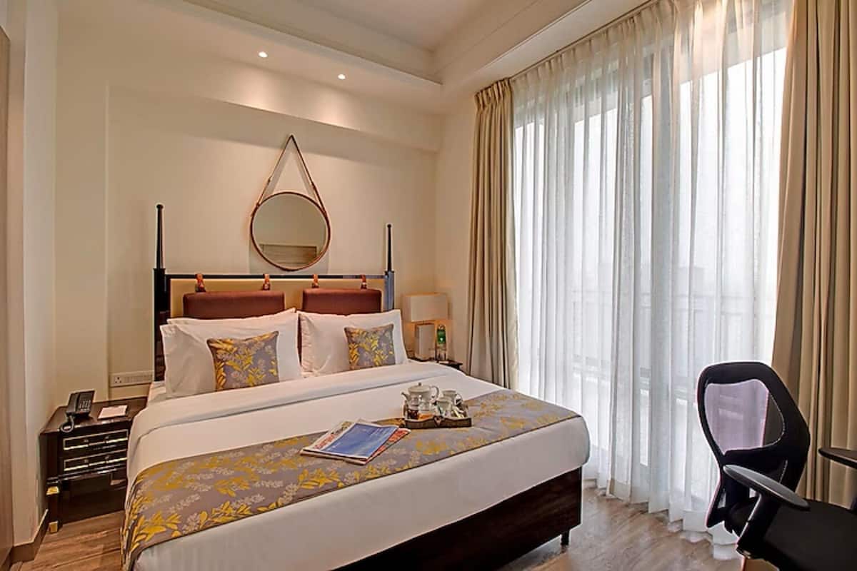 A hotel room with a large bed, bedside table, a chair, a mirror, and a window with curtains.