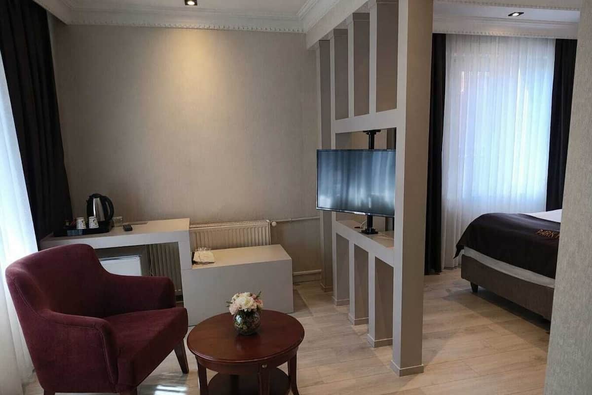 Ein Hotelzimmer mit einem Bett, einem Fernseher, einem Schreibtisch mit Stuhl, einem kleinen Tisch mit Blumen und einer Heizung.