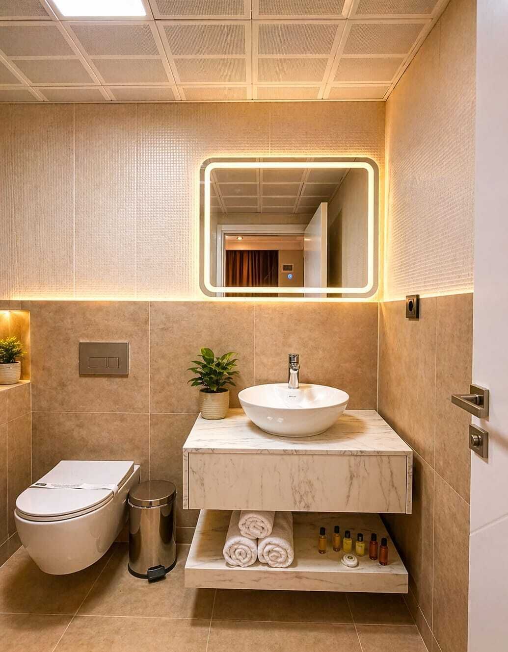 A modern bathroom with a white sink, mirror, and toilet. There are plants and toiletries on the counter.