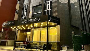 The exterior of the Ardos Park Hotel with a glass facade, outdoor seating area, and a signboard. - Ardos Park Hotel (Ankara)