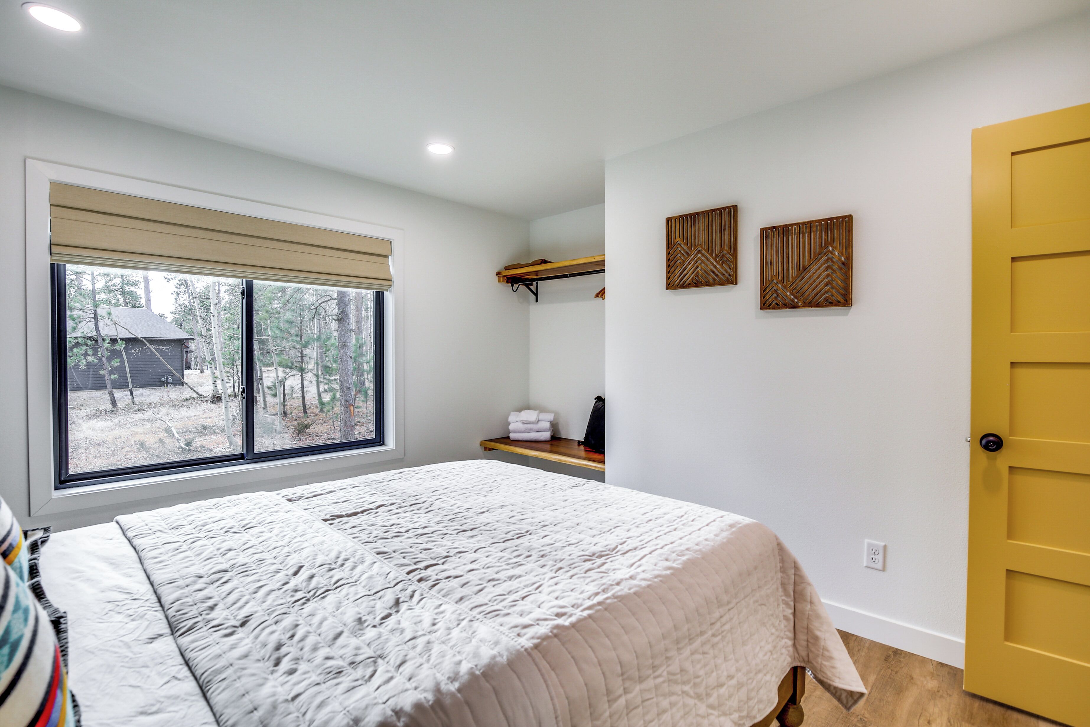 A bedroom with a large bed, a window with blinds, a wooden door, and two wall-mounted decorations.