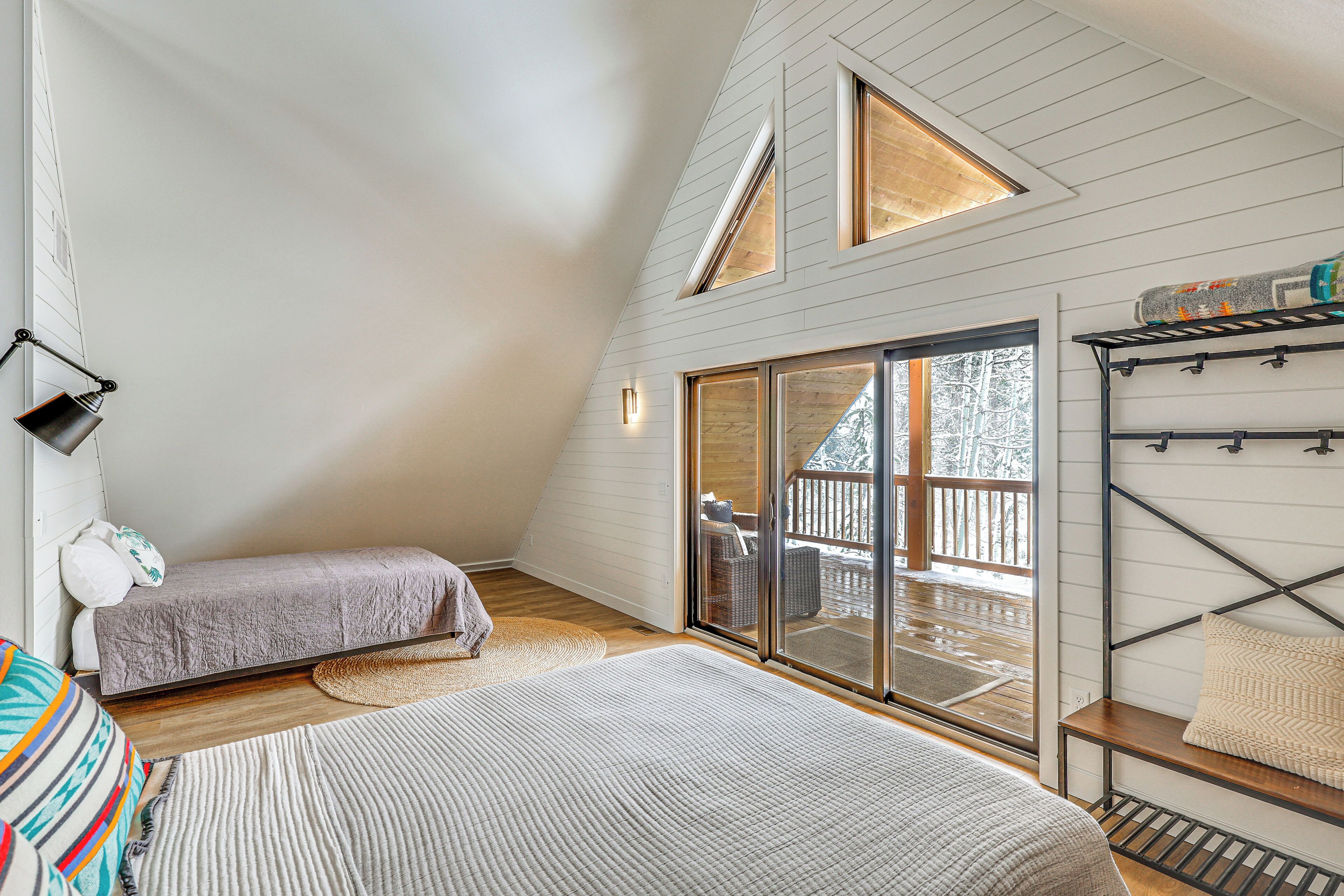 Ein gemütliches Schlafzimmer mit Schlafgalerie, einem großen Fenster mit Blick auf eine Holzterrasse und einer eingebauten Ablage mit Stauraum.