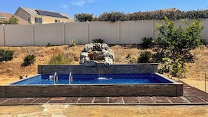Piscina retangular com cascata de pedra, rodeada por um deck de pedra e tijolos.