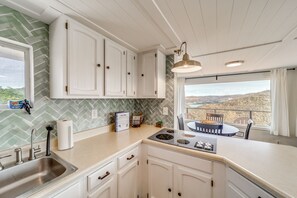 A kitchen with white cabinets, a stainless steel sink, a built-in stove, and a view of a mountainous landscape through a large window.