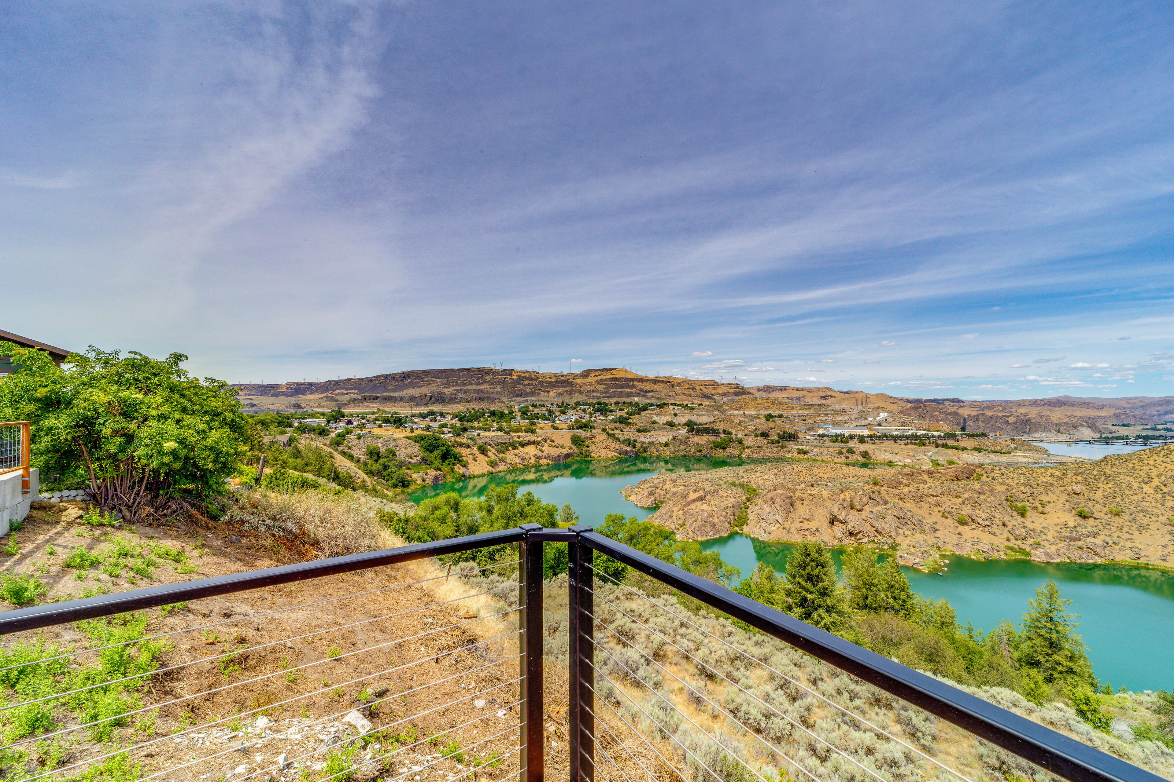 A scenic view from a balcony overlooking a river valley with distant hills and a clear sky.