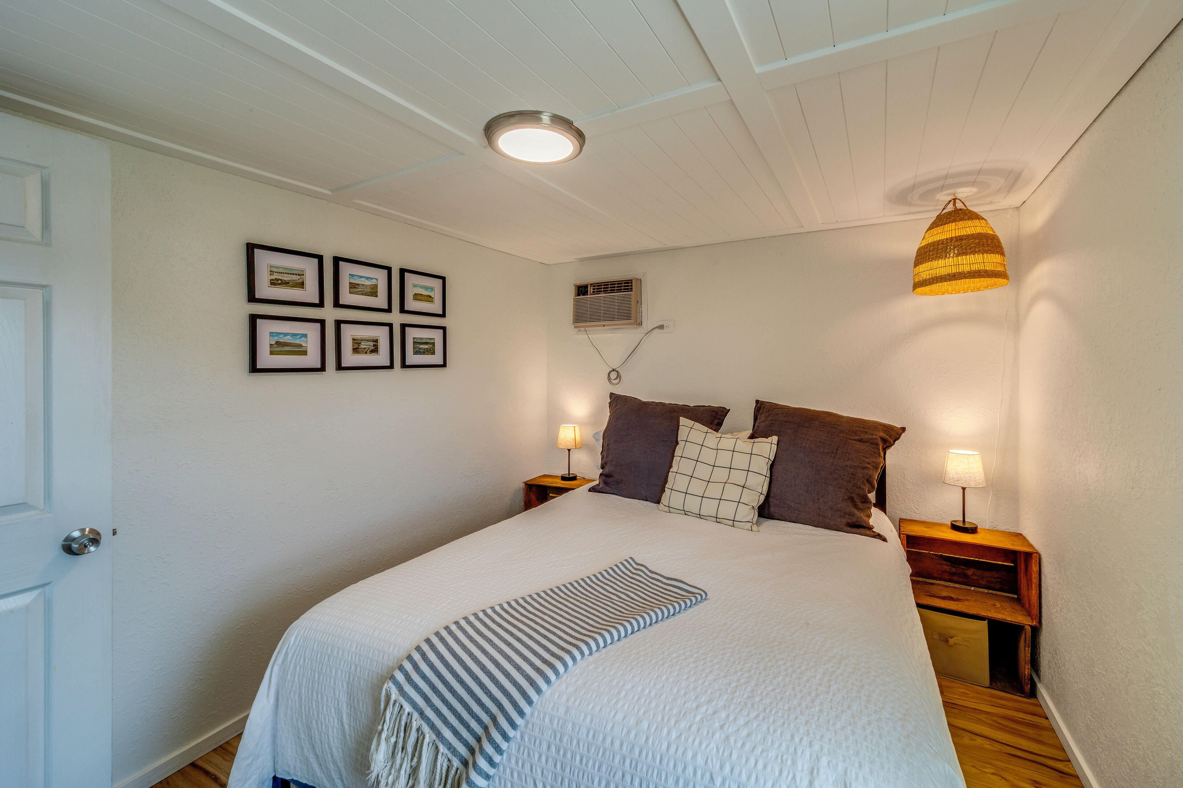A bedroom with a bed, two bedside tables with lamps, a ceiling light, and four framed pictures on the wall.