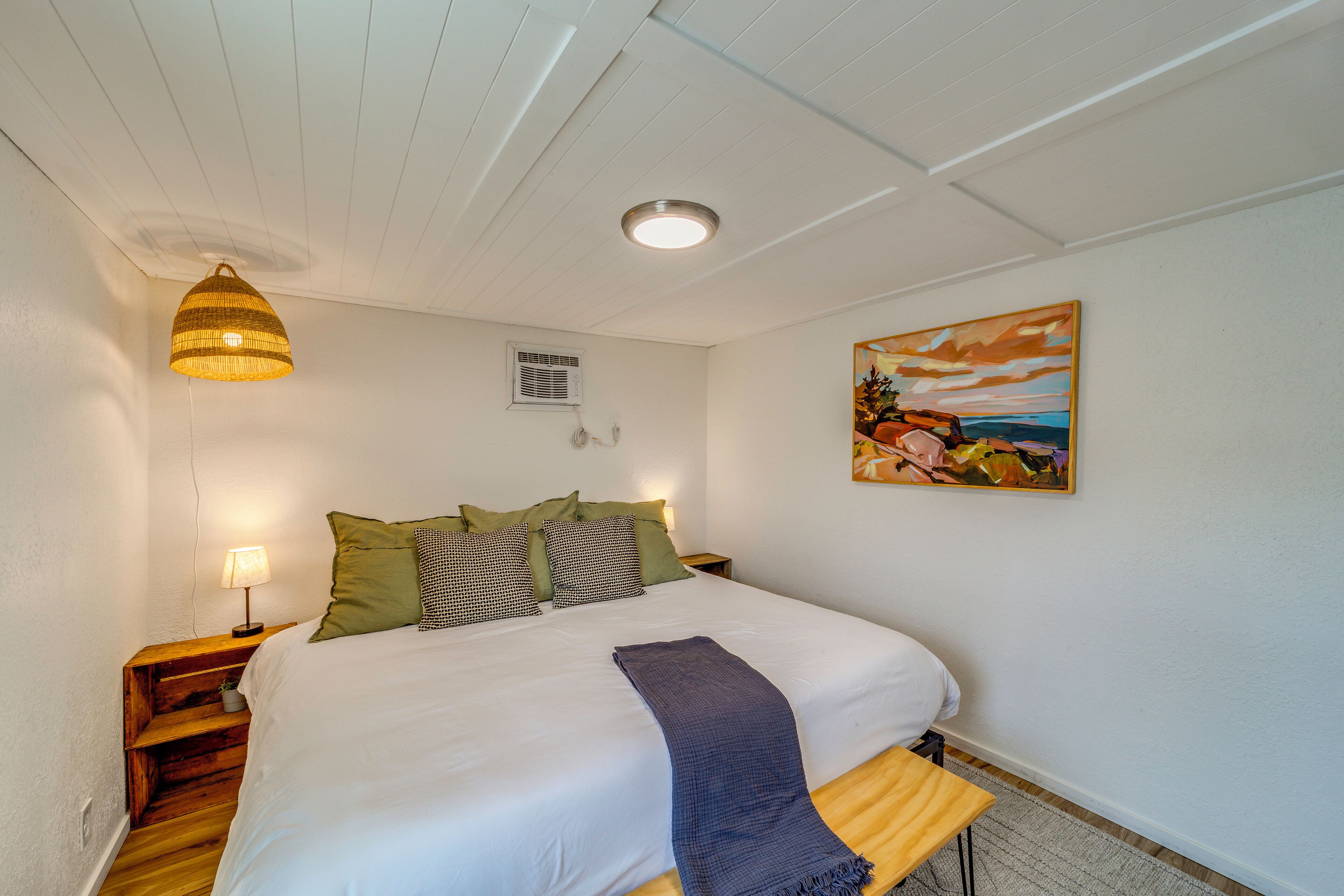 A bedroom with a bed, bedside lamp, artwork, and a ceiling light fixture.
