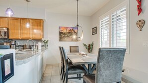 Une cuisine moderne avec des meubles en bois, un coin repas comprenant une table et des chaises, et une grande fenêtre avec des stores.