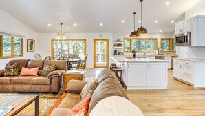 A spacious living room with a large sofa, a coffee table, and a dining area with a wooden table and chairs. The kitchen features white cabinets, a large island, and a microwave. - 4 Mi to Slopes: Family-friendly Stateline Home! (Stateline)