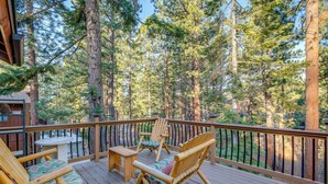 A wooden deck with two wooden chairs and a small table, surrounded by tall pine trees. - 4 Mi to Slopes: Family-friendly Stateline Home! (Stateline)