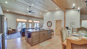 A spacious kitchen with wooden cabinets, a central island, and a dining area with a table set for four. - 'lavender Lodge' Mountain-view Pine Cabin w/ Deck (Pine)