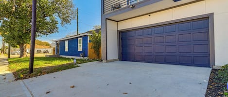 A two-story house with a blue garage door, a balcony with a metal railing, and a tree in the front yard.