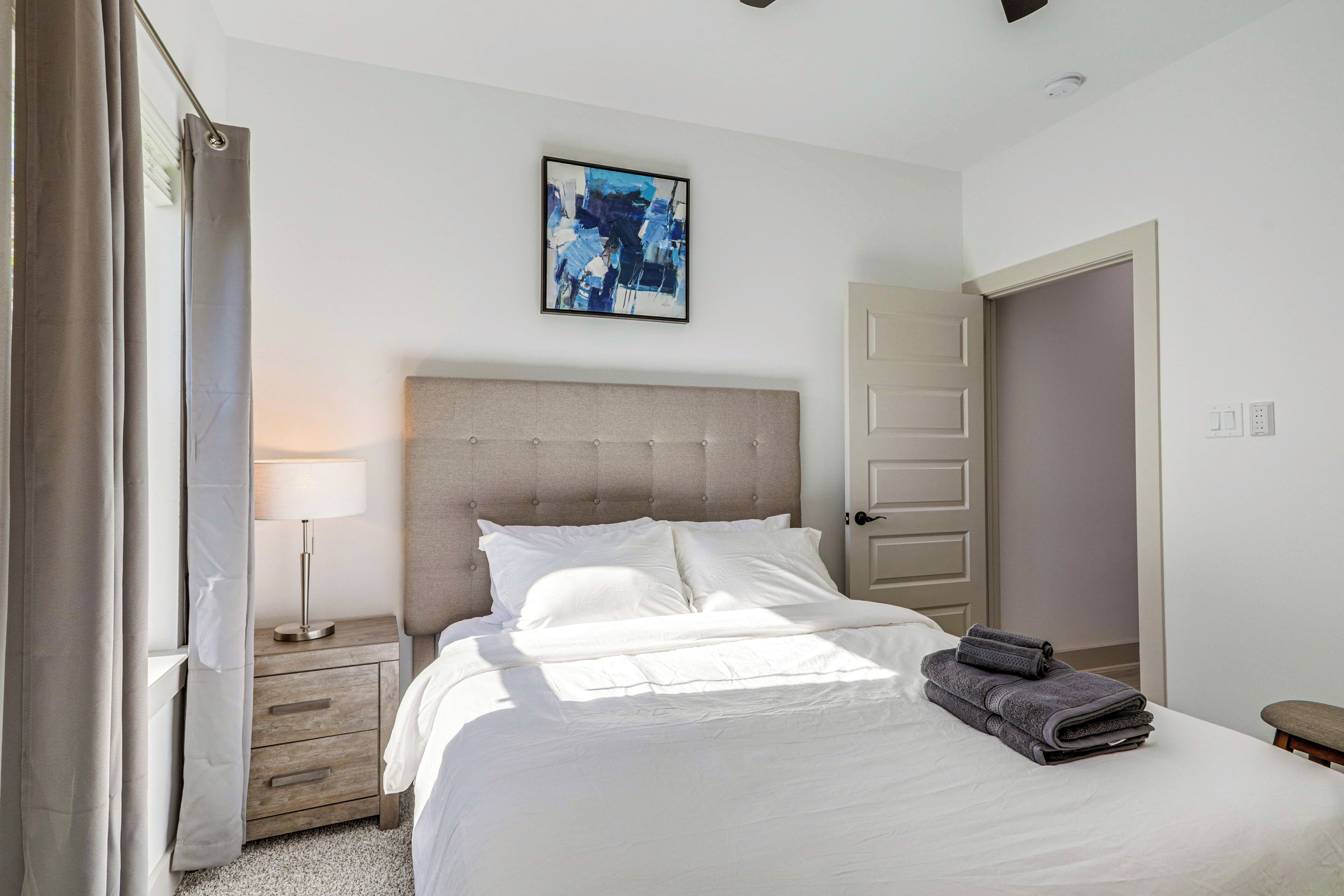 A neatly made bed with white linens, a grey headboard, and a folded grey towel on the side.