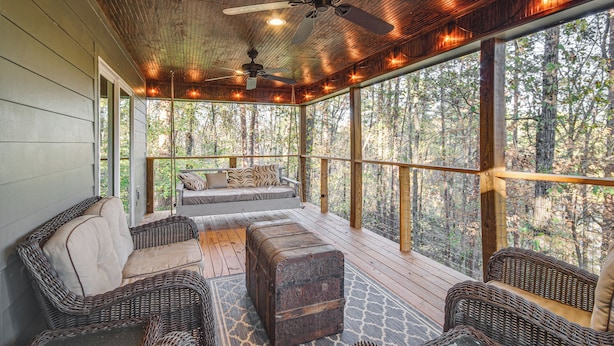 A covered outdoor seating area with wicker furniture, a ceiling fan, and a view of the forest. - Waterfront Home w/ 3 Decks, Fire Pits and Hot Tub! (Terry)