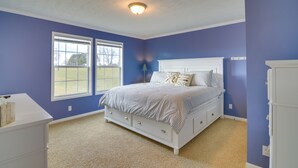Ein Schlafzimmer mit einem großen Bett, zwei Fenstern, einer Deckenleuchte und einer weißen Kommode.