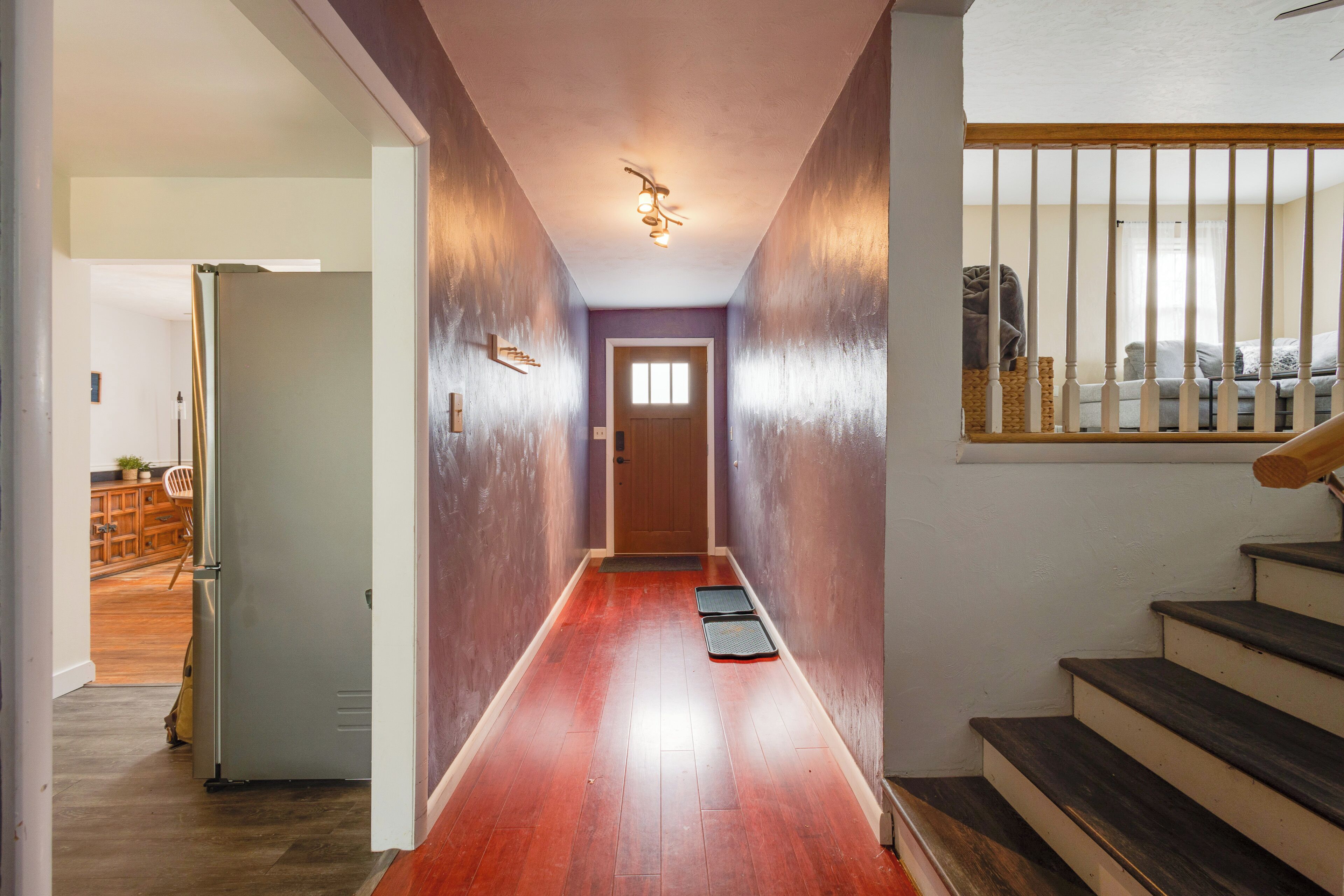 A hallway with a wooden floor, a door at the end, and a staircase with a railing.