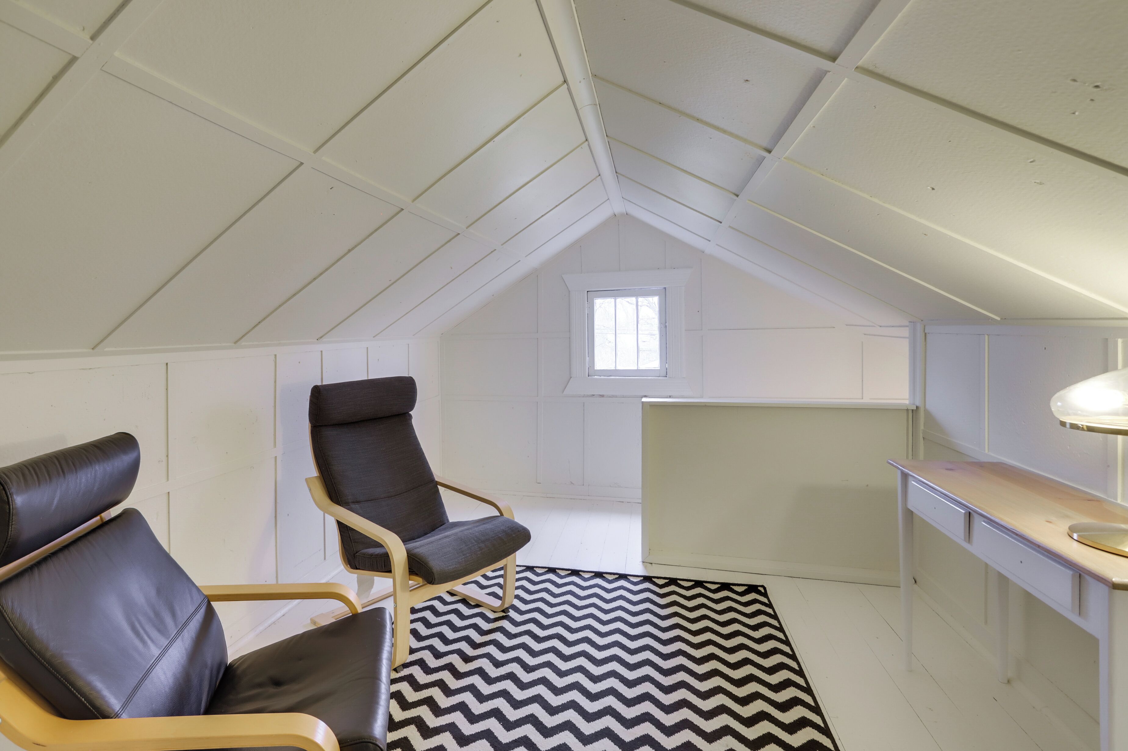 Une chambre aménagée dans les combles, avec deux fauteuils en cuir, un bureau et une grande fenêtre.