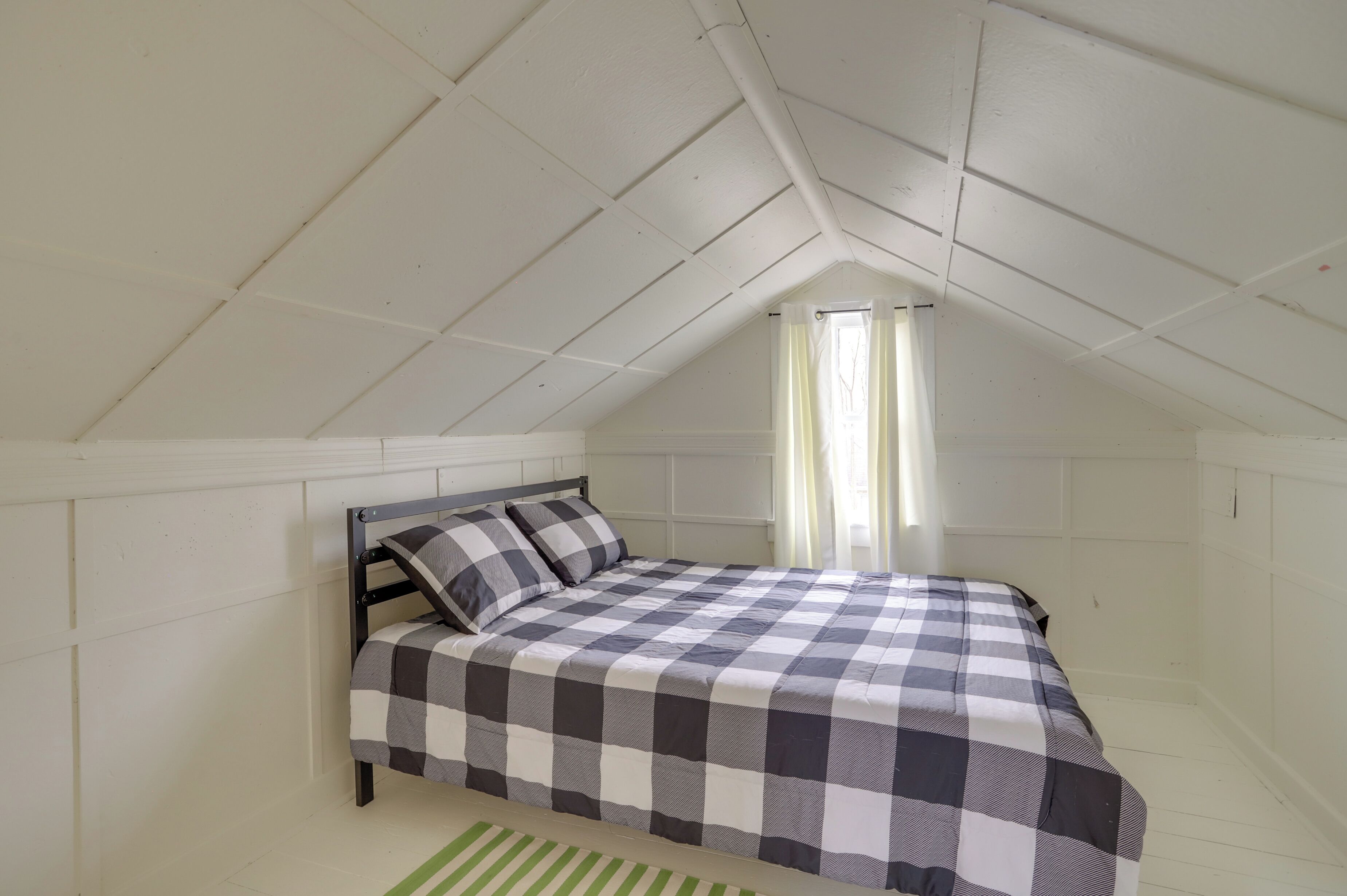 Ein Schlafzimmer mit kariertem Bettbezug, einem Holzkopfteil und einer schrägen Decke.