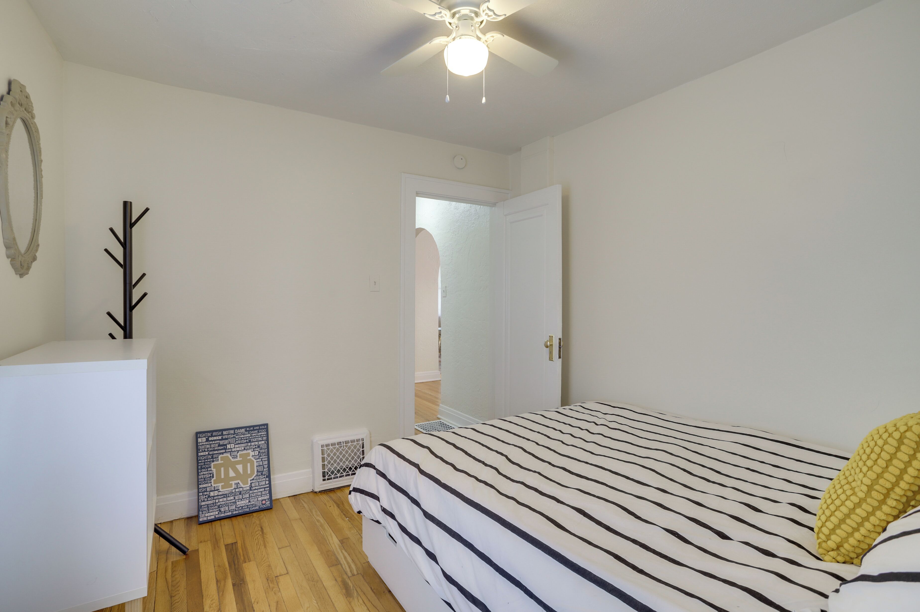 A bedroom with a bed, a white dresser, a ceiling fan, and a door leading to another room.