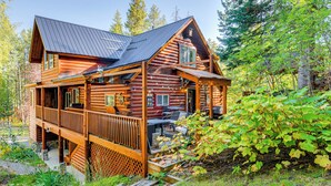 A log cabin with a porch and deck, surrounded by greenery.