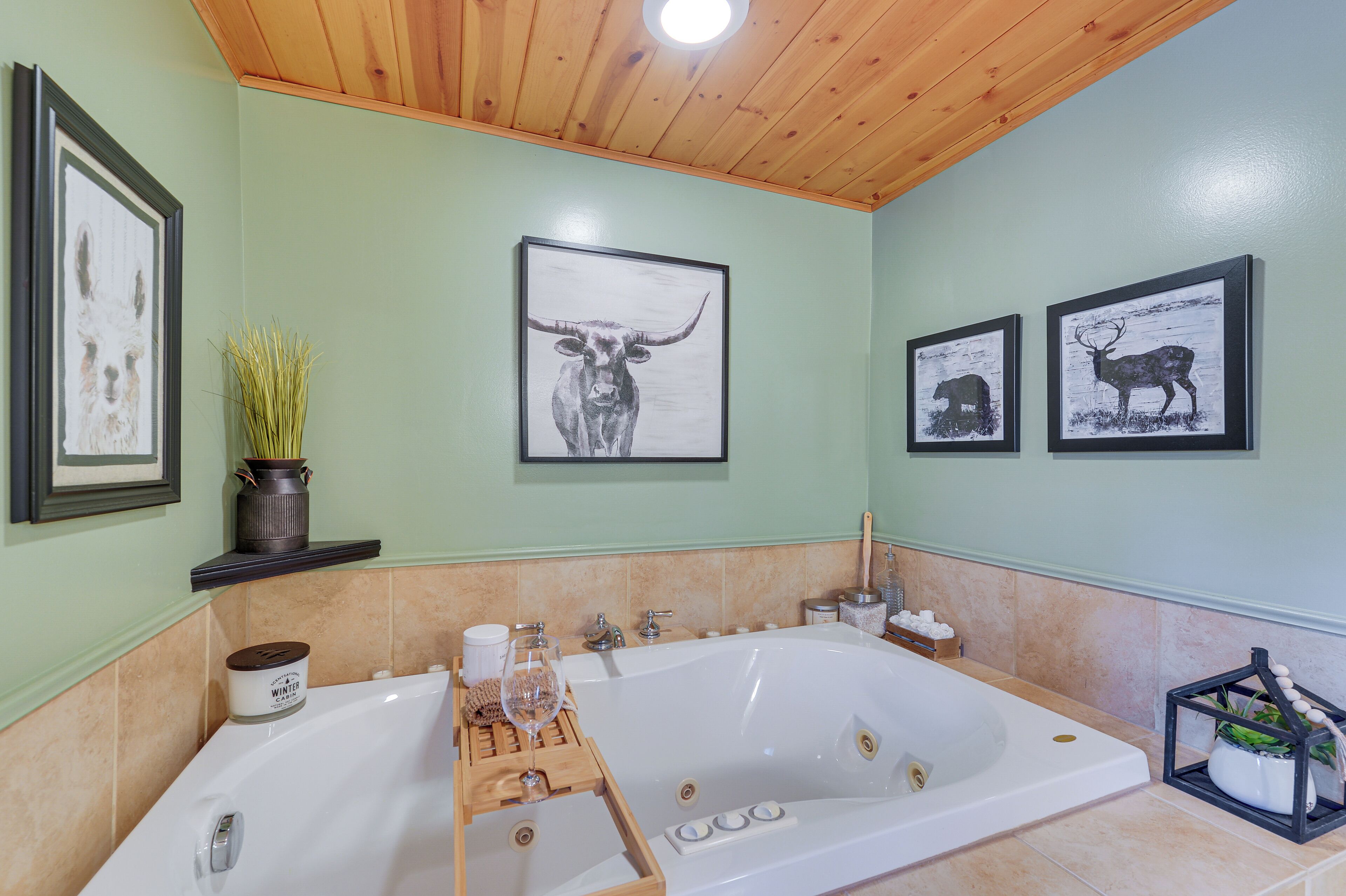 A bathroom with a large bathtub, framed artwork on the walls, and a wooden ceiling.