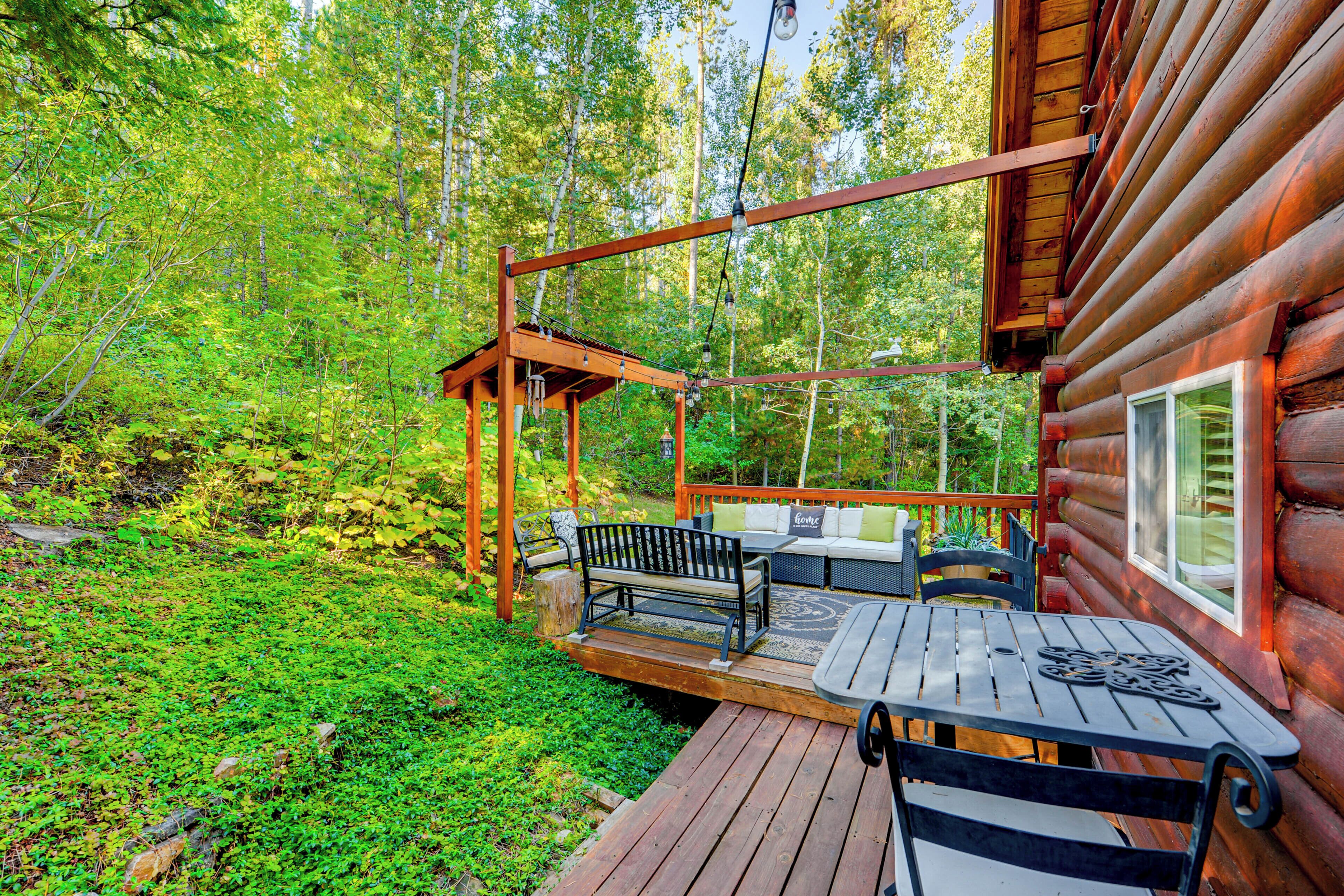 A wooden deck with outdoor furniture, surrounded by lush greenery.