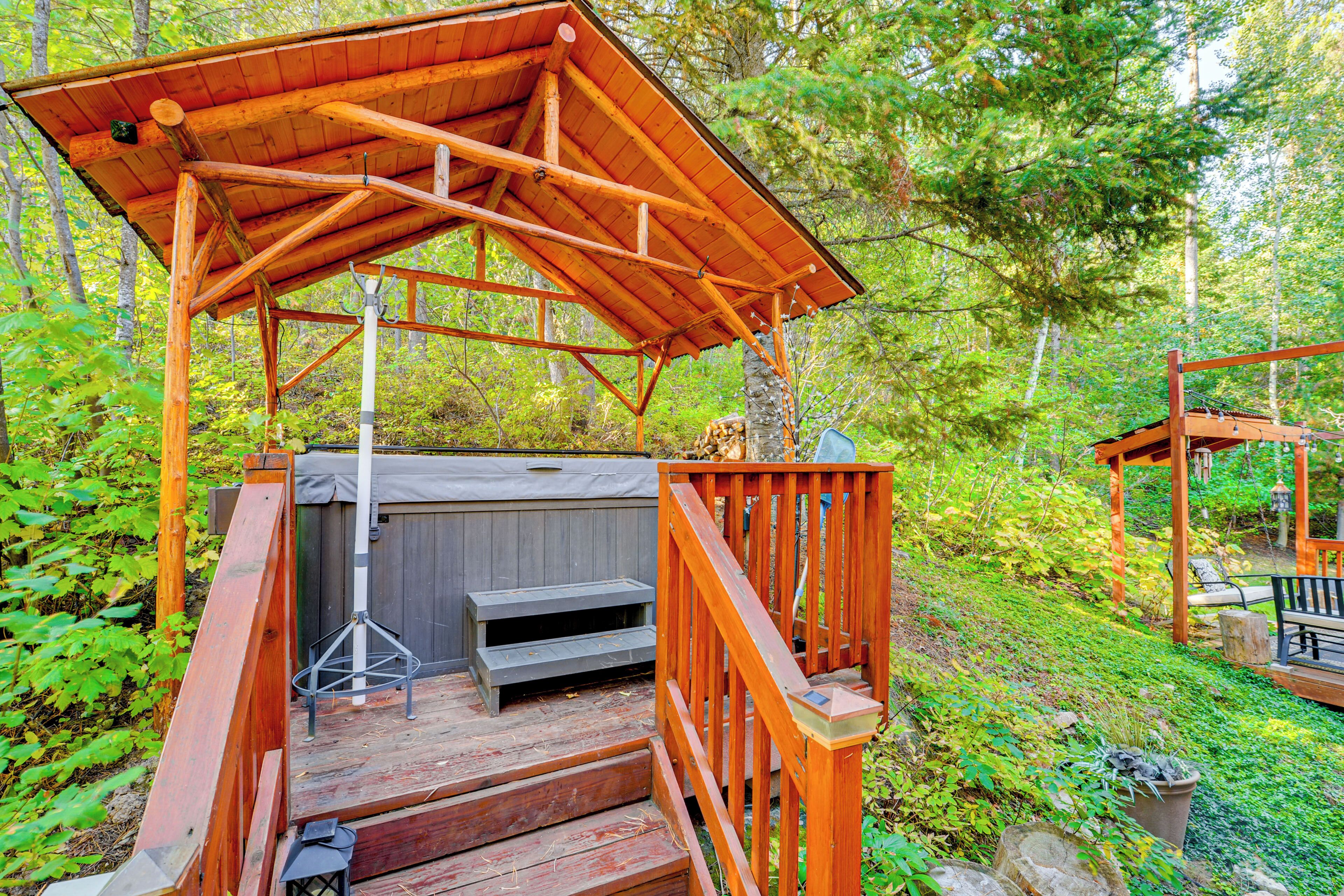Una terraza de madera con un jacuzzi y escalones que llevan a él, rodeada de abundante vegetación.