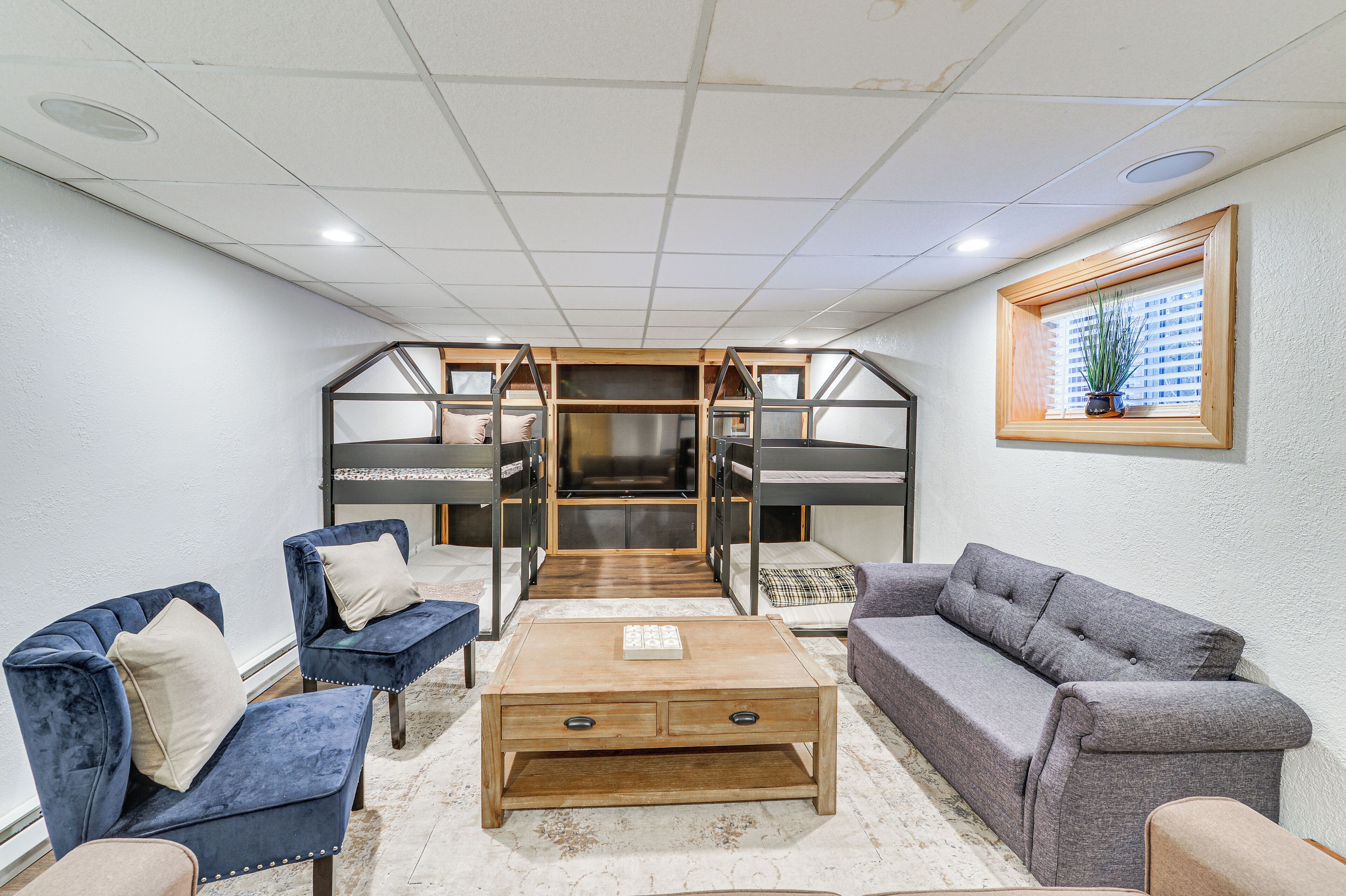 Una sala de estar moderna con un sofá, sillones, una mesa de centro y una cama litera con estructura de madera.