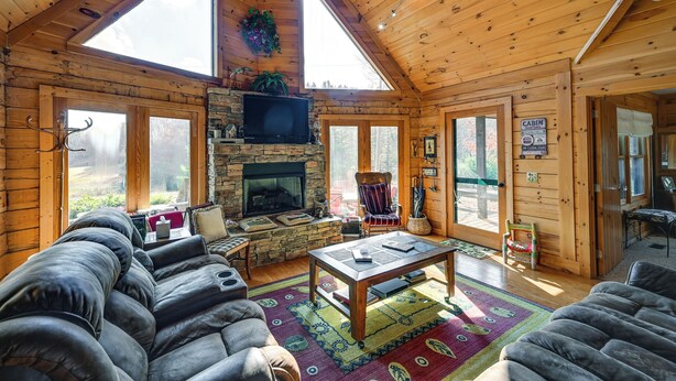 A log cabin interior with a stone fireplace, a television, and a cozy seating area. - Rustic Fancy Gap Cabin w/ Blue Ridge Parkway Views (Fancy Gap)