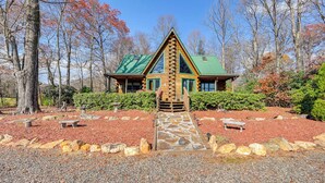 A log cabin with a green roof, surrounded by a landscaped garden with stone pathways and benches. - Rustic Fancy Gap Cabin w/ Blue Ridge Parkway Views (Fancy Gap)
