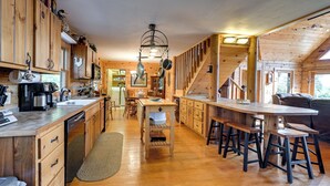 A spacious kitchen with wooden cabinets, a central island with stools, and a staircase leading to another level. - Rustic Fancy Gap Cabin w/ Blue Ridge Parkway Views (Fancy Gap)