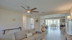 A spacious living room with a sofa, a ceiling fan, and a kitchen area in the background. - Game Room & Fire Pit: Family-friendly Aubrey Home (Aubrey)
