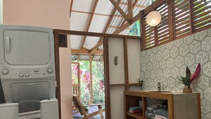 Une buanderie équipée d’un lave-linge, de rayonnages en bois et offrant une vue sur un jardin grâce à une porte en bois.