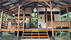 Une structure en bois surmontée d’un toit en métal, comprenant un espace cuisine et un coin salon avec un banc.