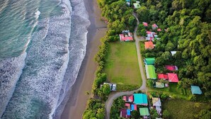 Vue aérienne d’une zone côtière avec une plage et un ensemble de maisons colorées, entourées d’une végétation luxuriante.