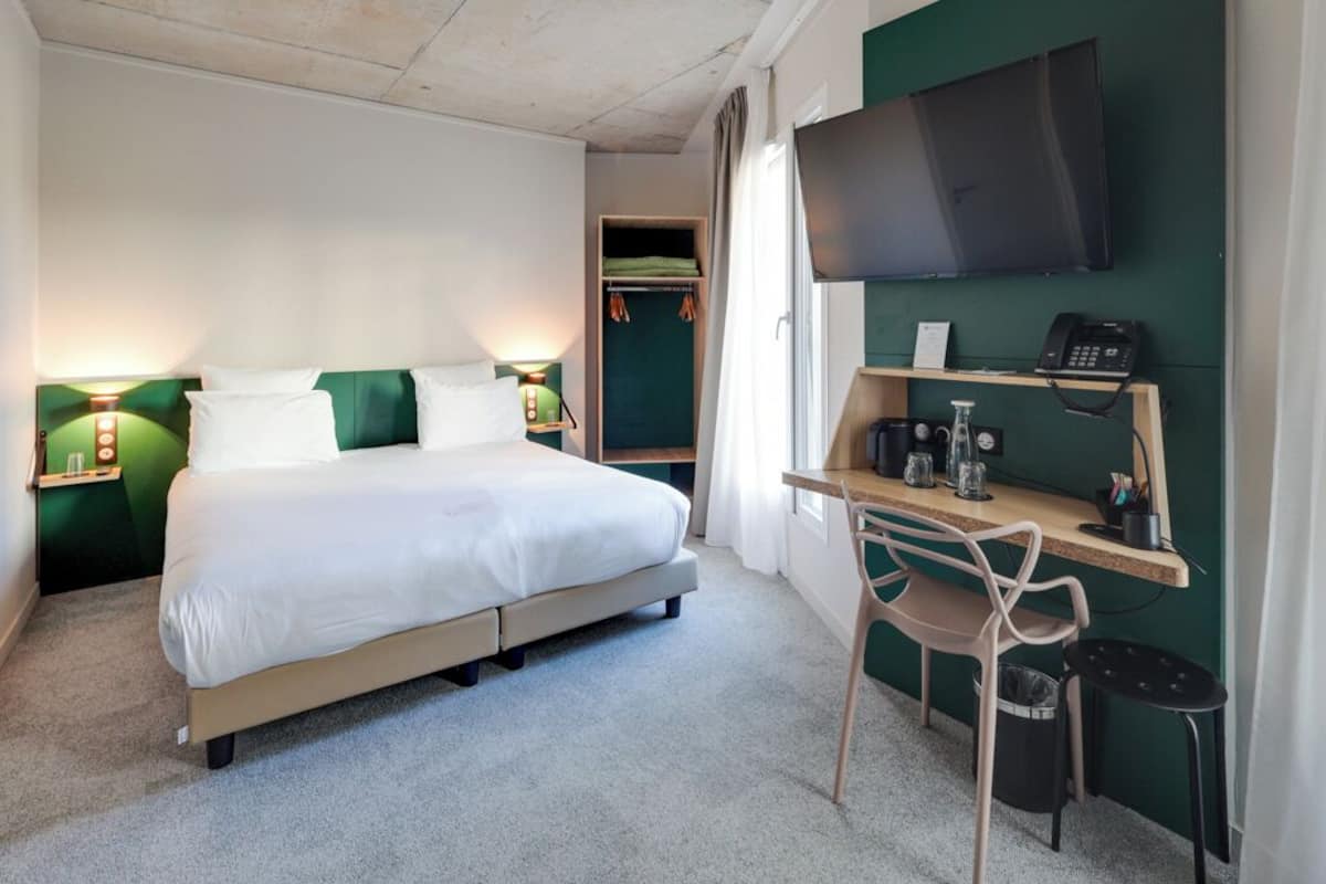 A hotel room with a bed, bedside lamps, a desk with a chair, a TV, and a telephone.