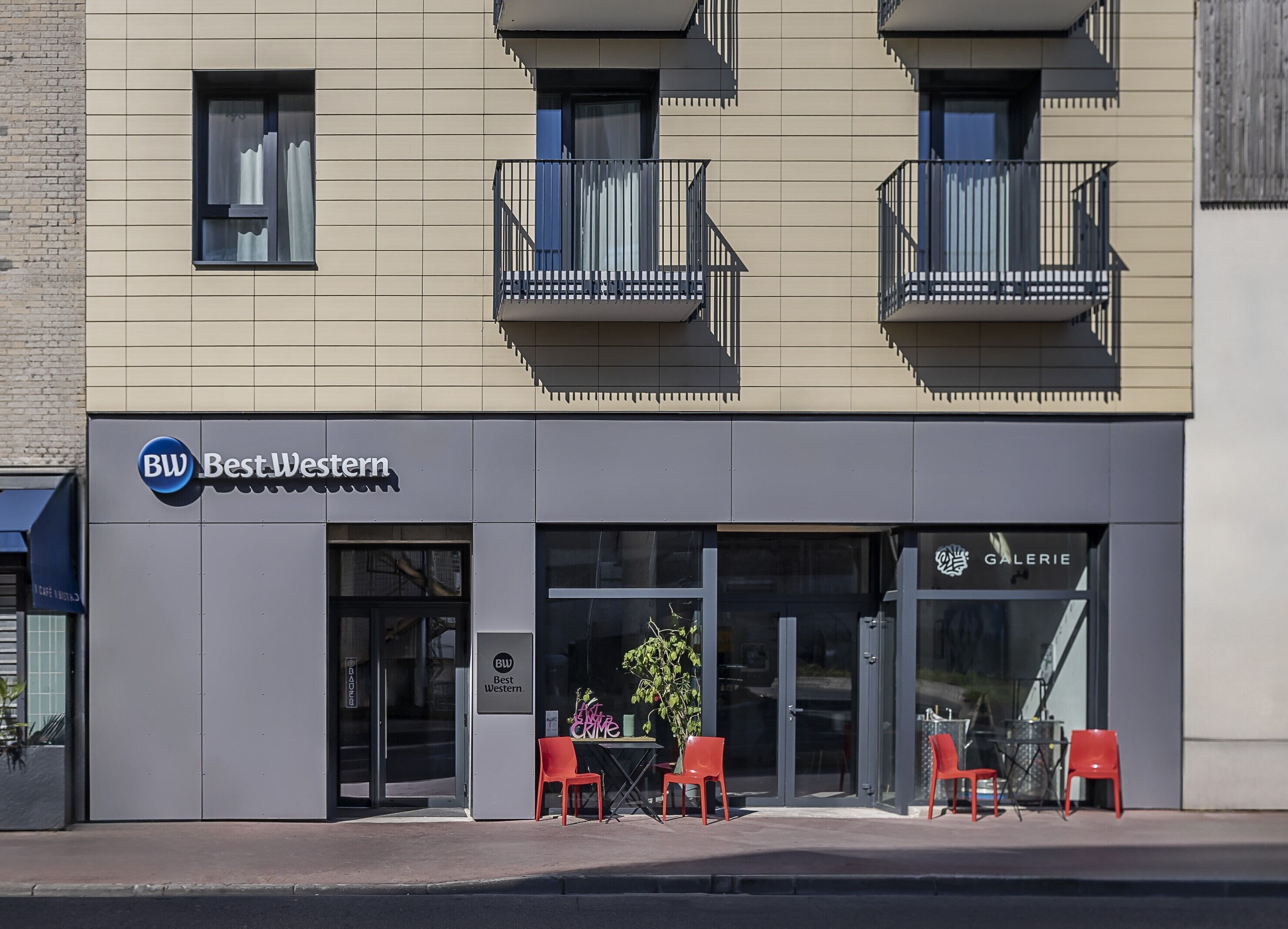 Un bâtiment sur lequel on peut lire l’inscription « BW BestWestern », avec une devanture composée d’une porte vitrée et de chaises rouges placées à l’extérieur.