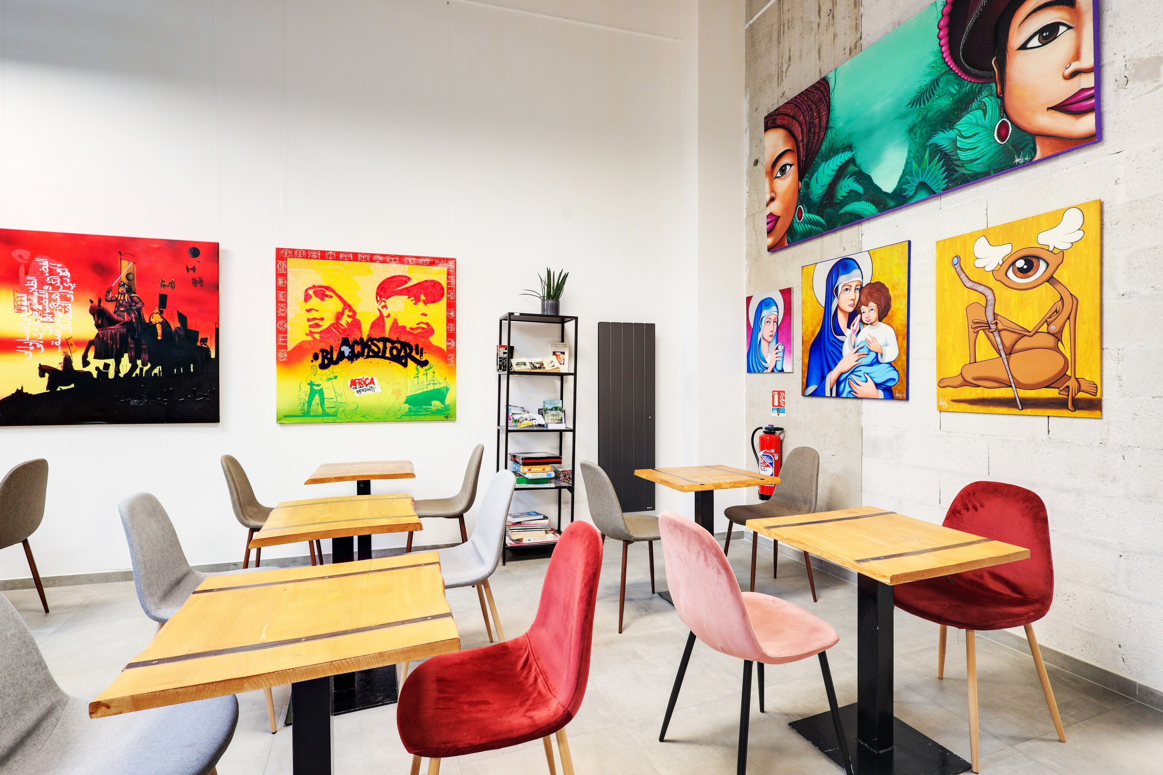 A modern dining area with wooden tables and chairs, a bookshelf, and artwork on the walls.