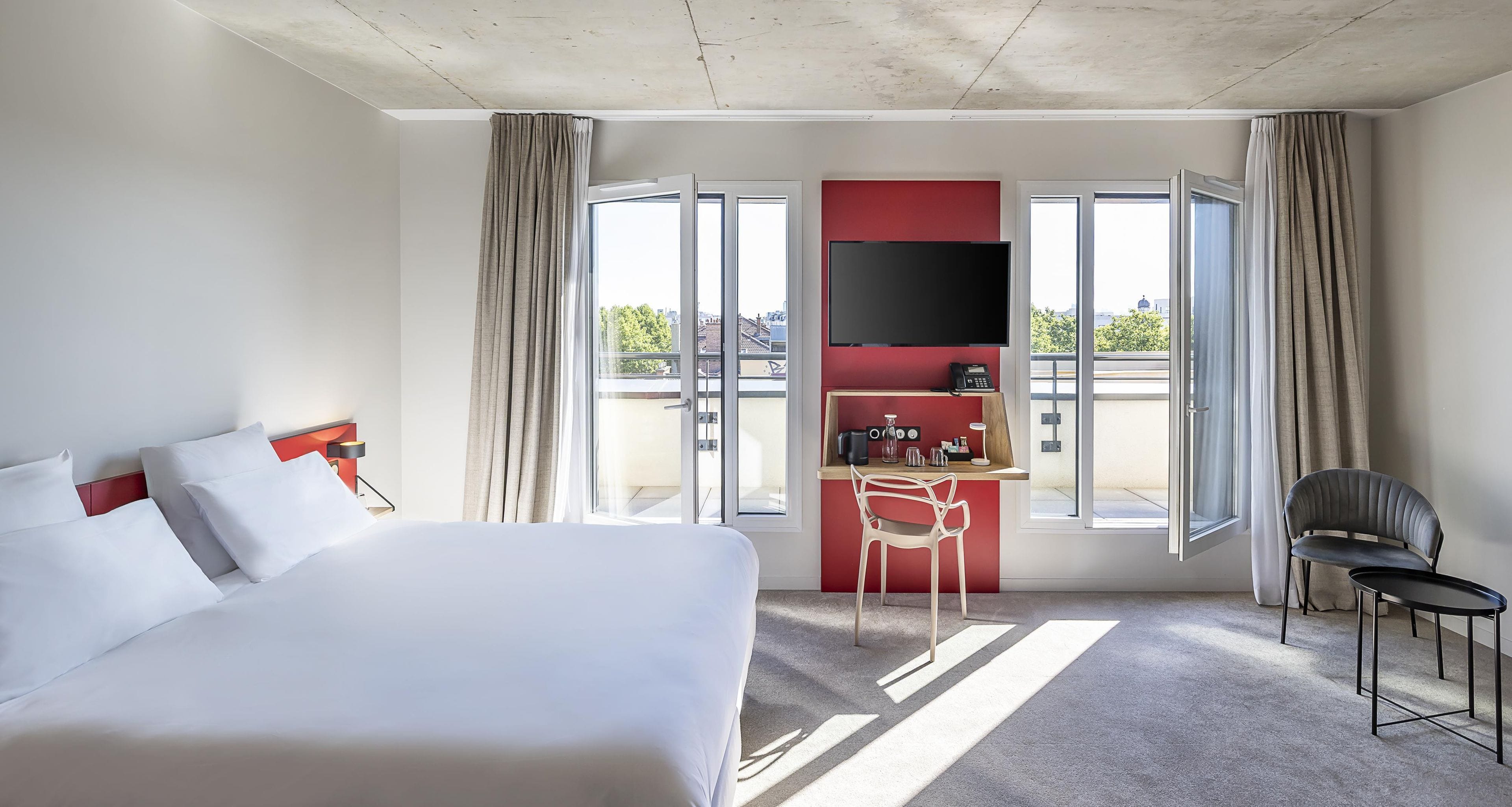 Habitación de hotel con cama, escritorio, silla, televisor y vista a la ciudad.