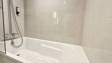 Un baño moderno con una bañera independiente, un cabezal de ducha manual y un grifo de pared.