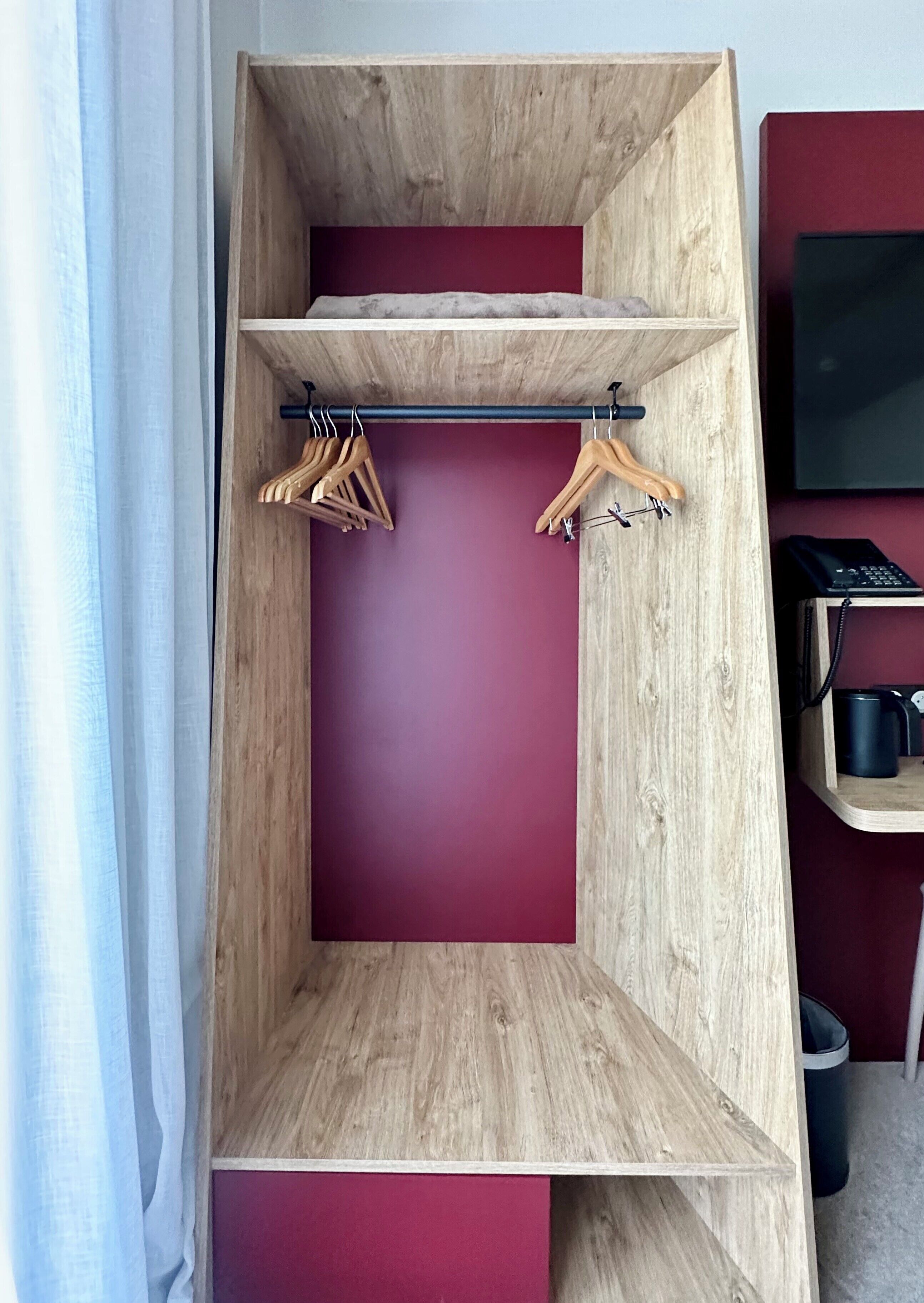 Ein Zimmer mit einem Holzschrank, einer roten Akzentwand und einem schwarzen Telefon auf einem kleinen Tisch.