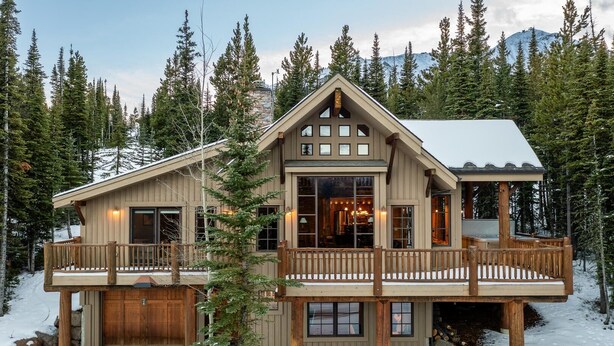 Une cabane en rondins à deux étages, dotée d’un balcon, entourée de neige et d’arbres.