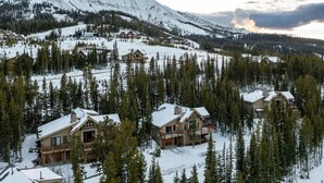 Une station de montagne enneigée, avec plusieurs bâtiments d’hébergement, entourée de forêts denses et de pentes recouvertes de neige.
