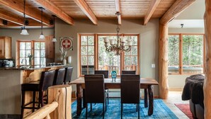 Un coin repas rustique avec une table et des chaises en bois, de grandes fenêtres et un lustre.