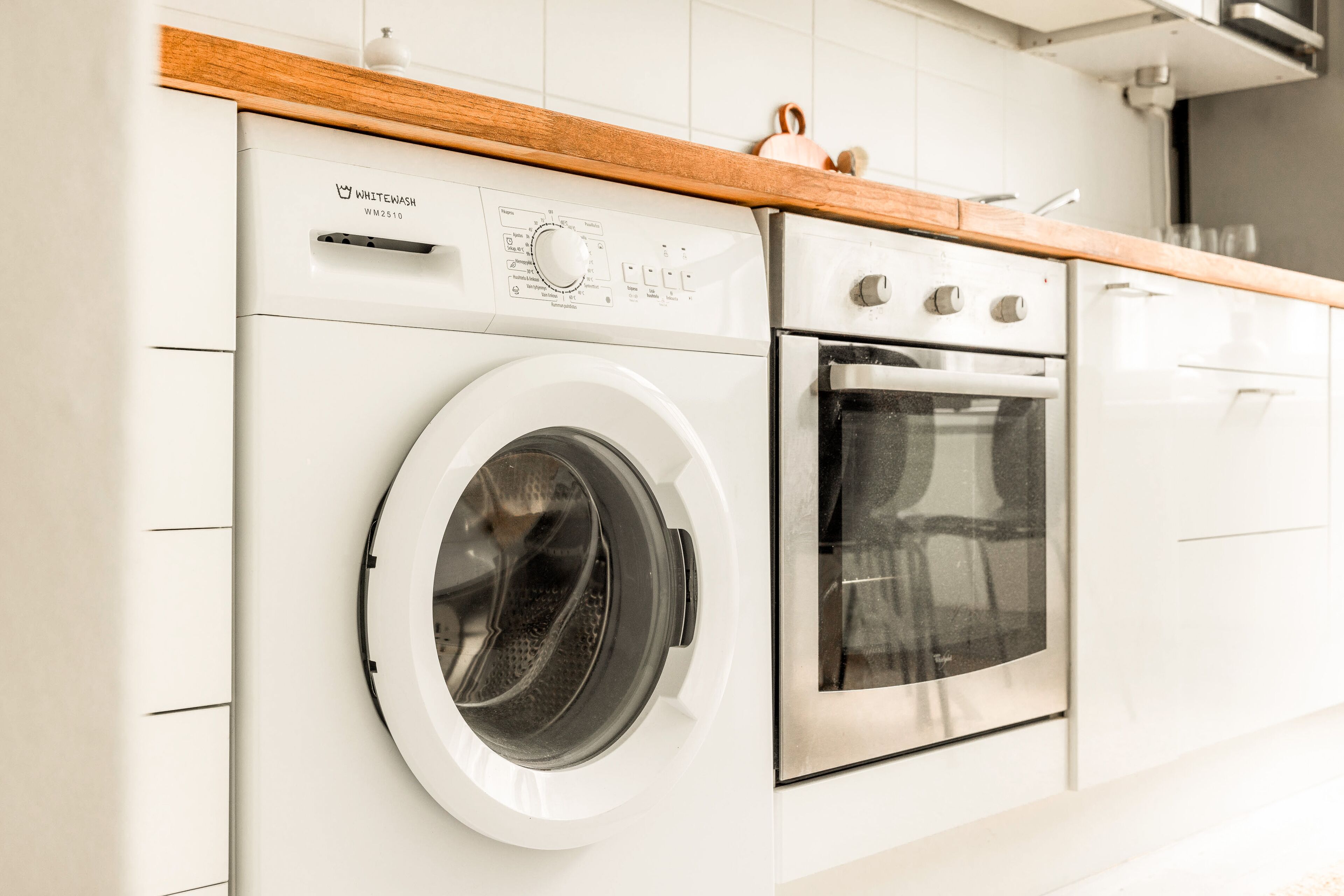 Una cocina compacta con lavadora y secadora integradas, encimera de madera y electrodomésticos de acero inoxidable.
