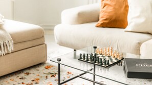 Um tabuleiro de xadrez sobre uma mesa de vidro em uma sala de estar com um sofá e almofadas.