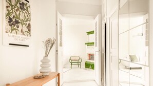 Um corredor com um banco de madeira, uma cadeira verde e um vaso branco com plantas secas.