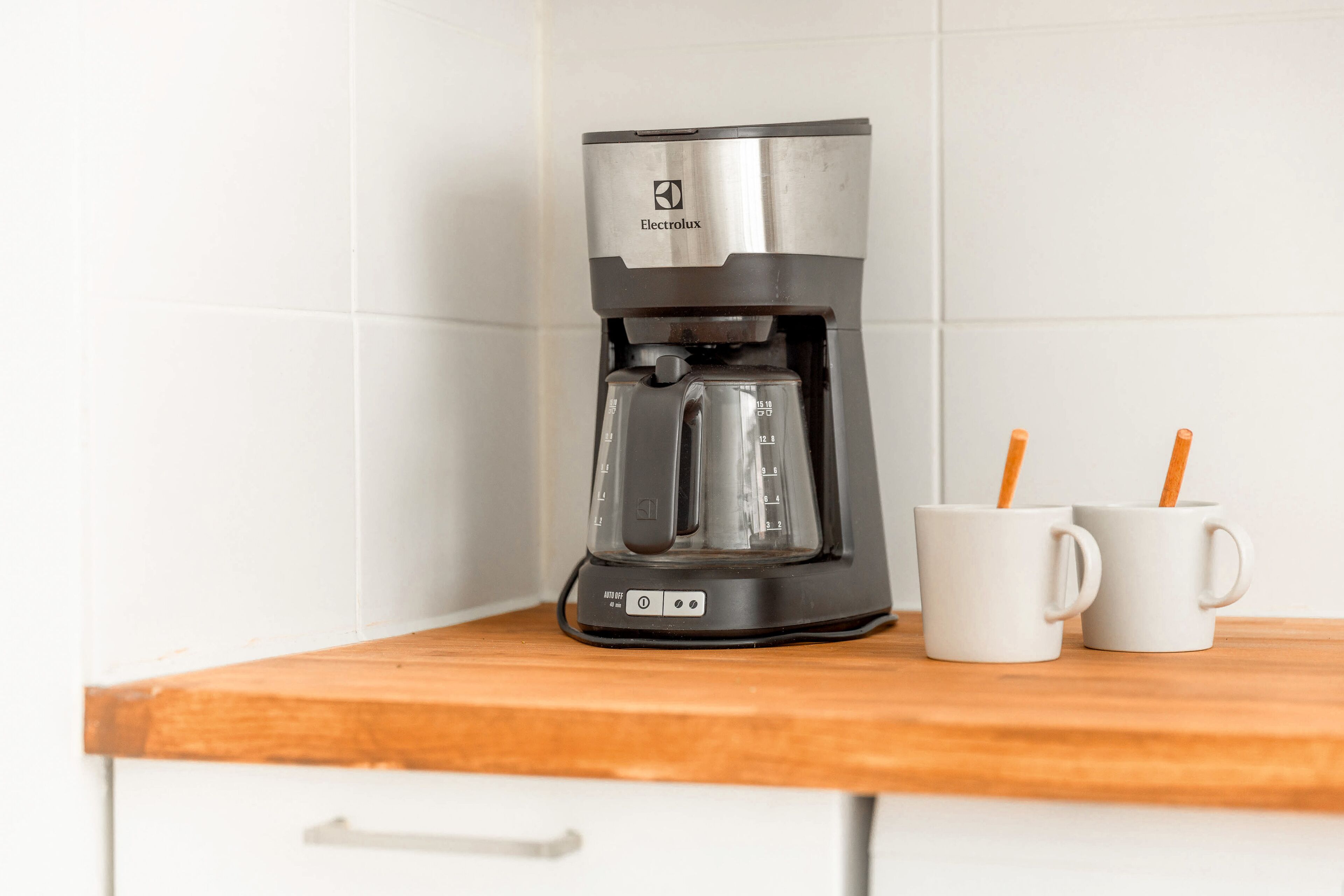 A coffee maker on a wooden countertop with two white mugs beside it.